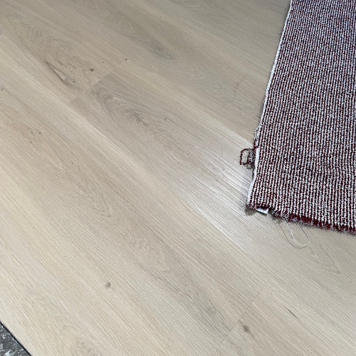 Gerafelde roodbruine vloerkleedrand op lichte houten vloer