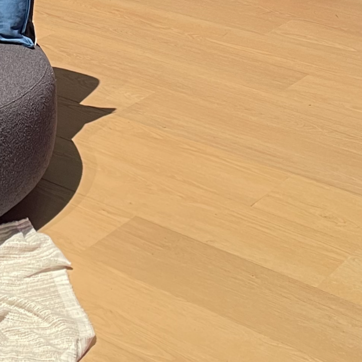 Houten vloer naast bruine poef en licht kleed