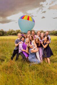 Vrolijke vriendengroep poseert voor kleurrijke luchtballon in grasveld