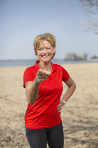 Lachende vrouw in rood shirt wijst op strand