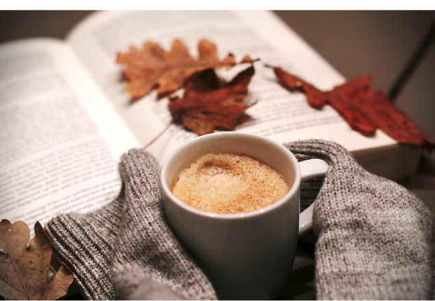 Warme koffie, wollen handschoenen en open boek met herfstbladeren