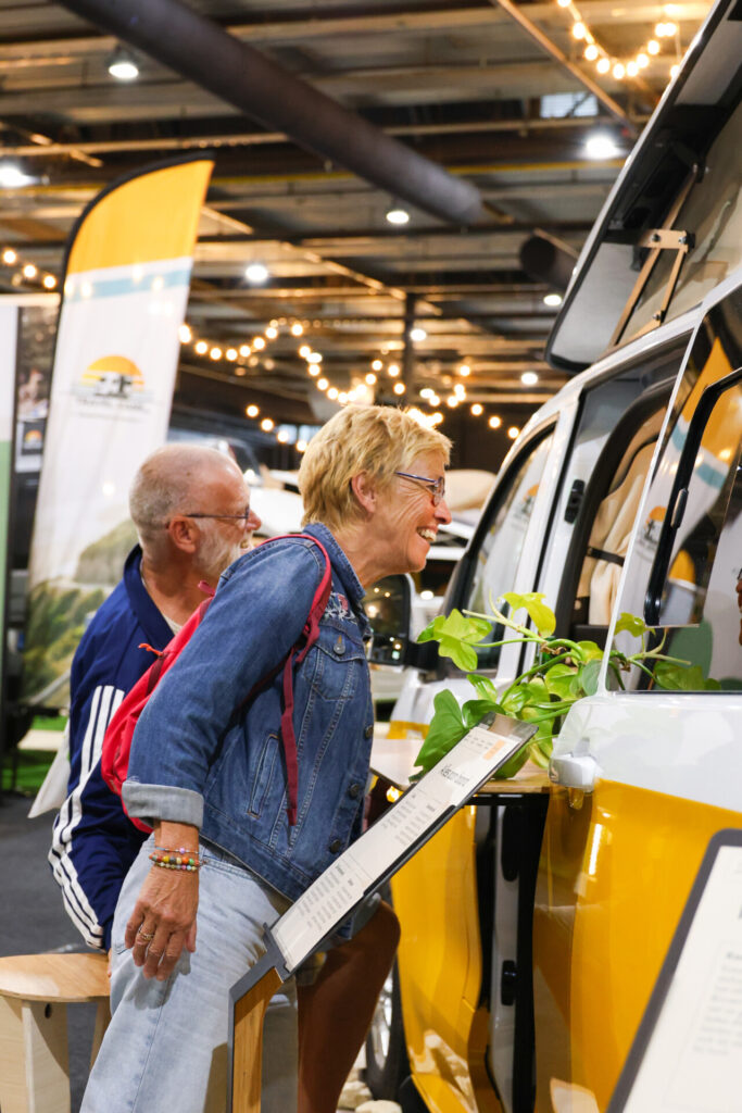 Bezoekers bekijken gele camper op een beurs