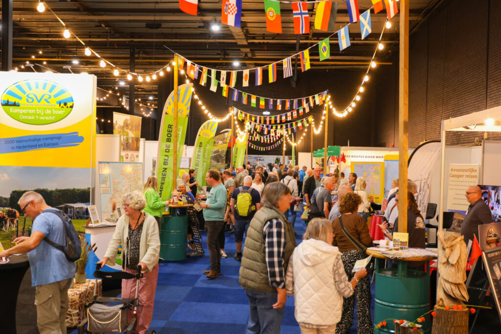 Bezoekers op kampeerbeurs met internationale vlaggen en stands