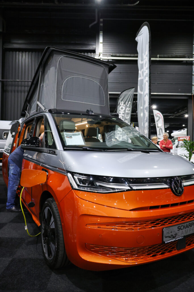 Oranje Volkswagen camper met geopend hefdak op beurs