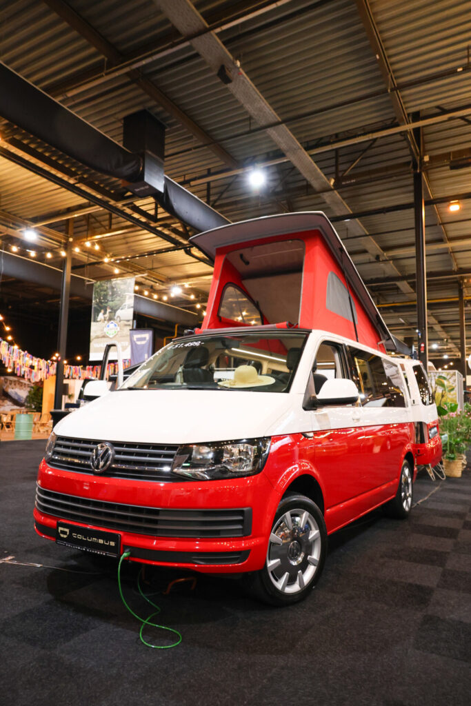 Rood-witte Volkswagen camper met uitgeklapt hefdak op beurs