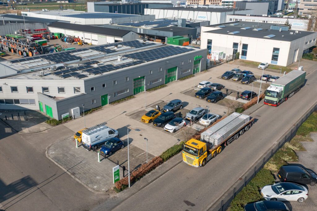 Luchtfoto van industriepand met zonnepanelen, parkeerplaats en vrachtwagens