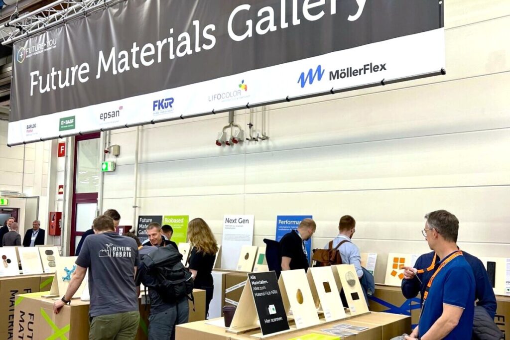 Über der Future Materials Gallery hängt das große Banner, auf dem die teilnehmenden Unternehmen präsentiert werden.