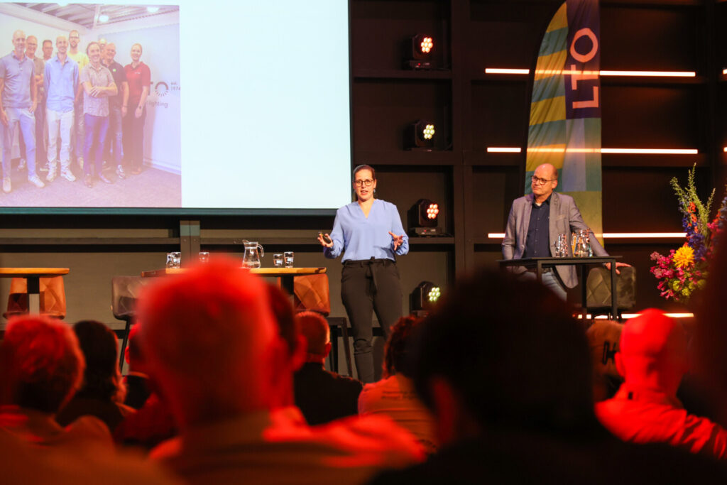 Sprekers presenteren op verlicht podium voor publiek