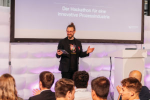 #speaker in Nahaufnahm spricht und steht vor der LEinwand, Publikum ist von hinten zu sehen