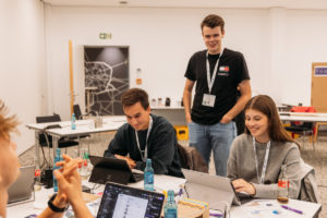 Teilnehmer sitzen an Tischen im Seminarraum und arbeiten am Projekt, von vorn fotografiert