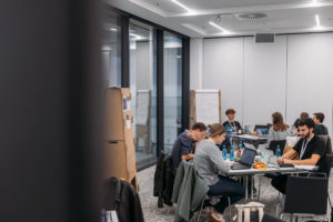 Teilnehmer sitzen an Tischen im Seminarraum und arbeiten am Projekt, von hinten fotografiert