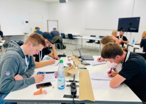 Teilnehmer sitzen an Tischen im Seminarraum und arbeiten am Projekt, von der Seite fotografiert