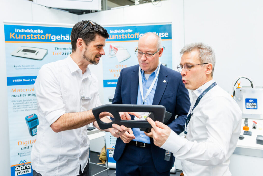 Drei Männer unterhalten sich über ein Kunststoffprodukt in ihrer Hand auf der KPA Ulm 2025