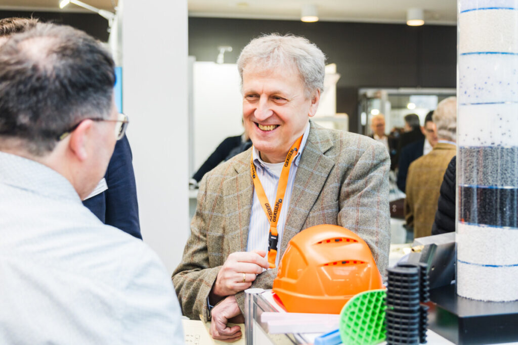 Fachbesucher auf der KPA 2026 in Ulm, l&auml;chelnd im Gespr&auml;ch mit einem Aussteller vor mehreren Kunststoffprodukten.