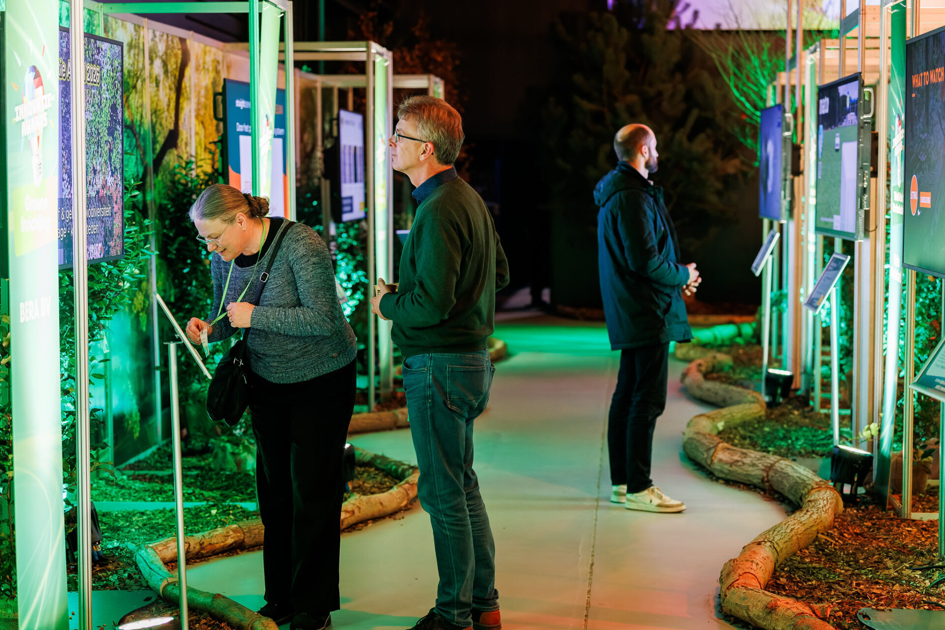 Bezoekers bekijken interactieve schermen in groen verlichte expositie
