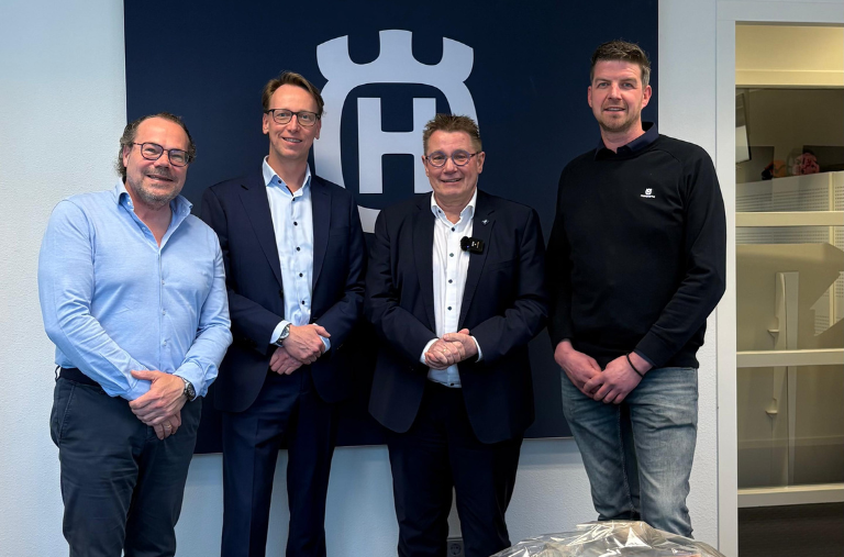 Vier mannen poseren voor Husqvarna-logo op kantoor