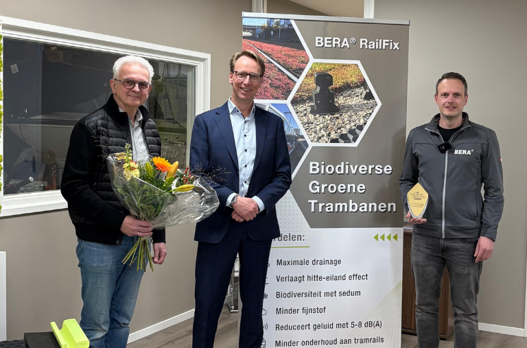 Drie mannen bij BERA RailFix-banner met bloemen en award