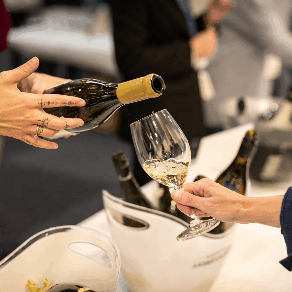 Hand som håller i vinflaska häller upp vin till gäst