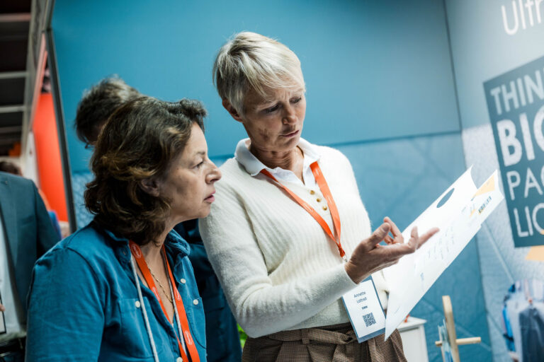 Twee vrouwen bekijken brochure op beursstand