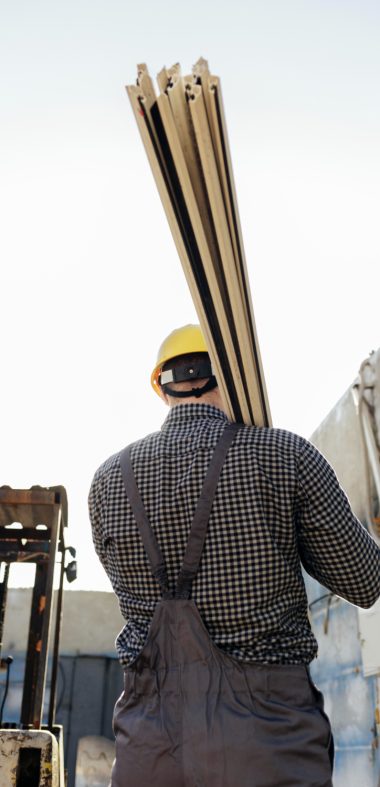 Man op een werf met planken op zijn schouders