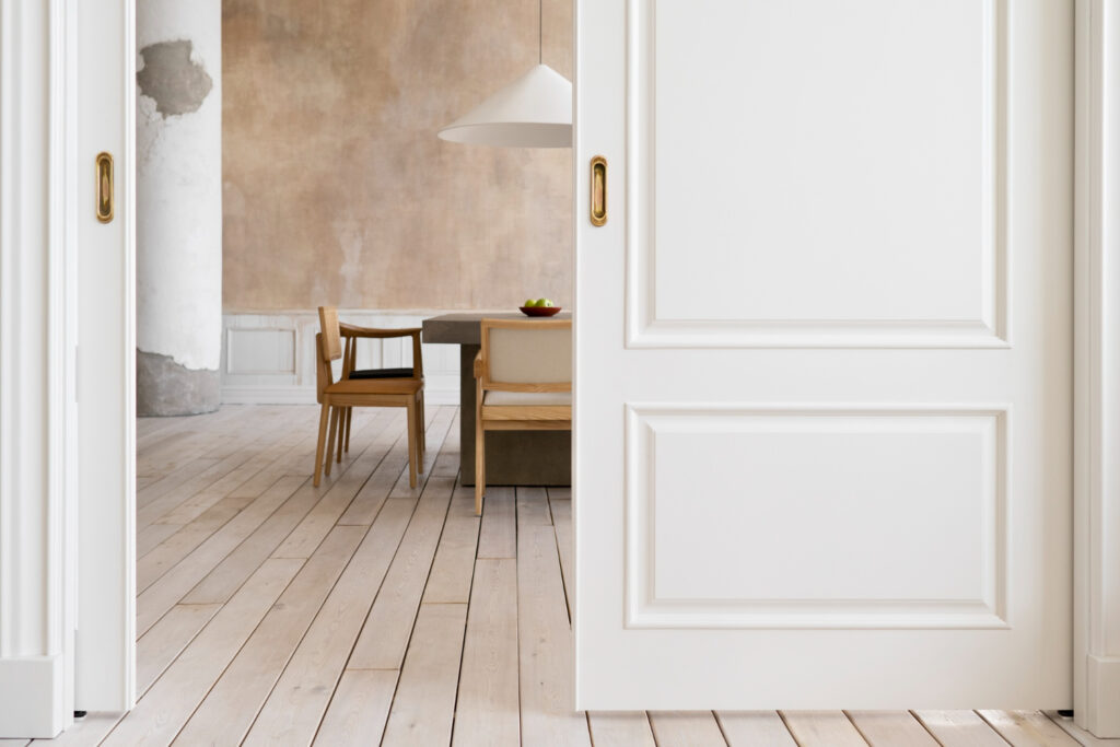 Witte schuifdeuren met gouden deurbeslag. Daarachter ene eetkamer.