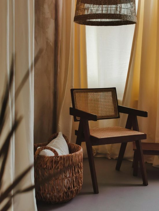 Hoek van een woonkamer met een houten stoel en een houten mand. Alles in warme tinten.
