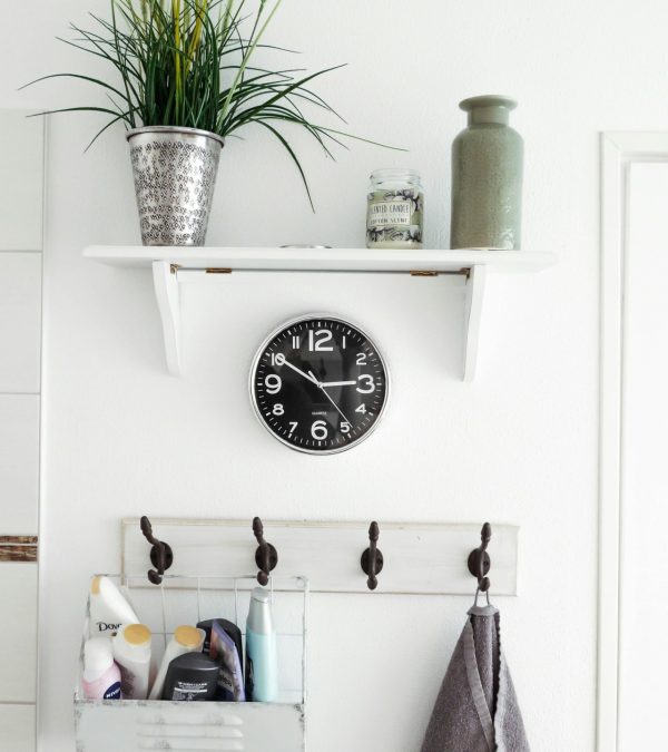 Baden voor mensen met mobiliteitsproblemen Interieurdetails in een badkmamer. Een rekje met een plant en vaas op. Een klok aan de muur en hieronder een kapstok met douchespullen.
