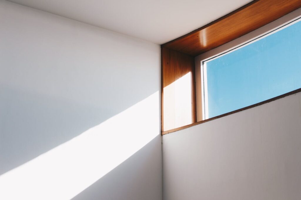 Een afbeelding van de hoek van een kamer, waar een raam een lichtstraal doorlaat. De lucht is blauw en het raamkozijn is van hout.