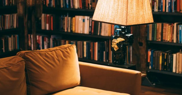 Een kamer in geel licht met een muur vol boekenkasten. Daarvoor bevindt zich een mosterdgele zetel met een retro staanlamp ernaast.