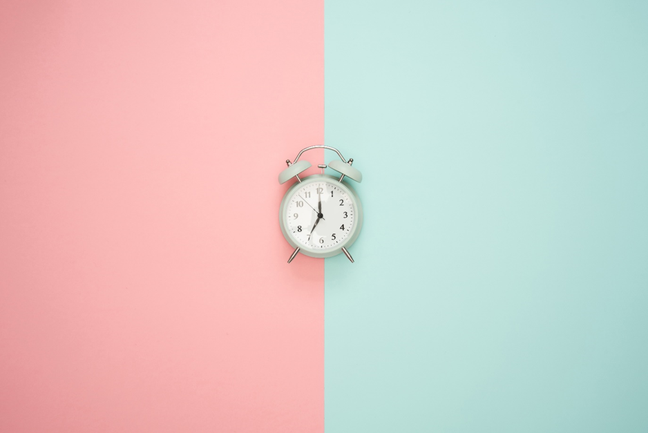 wekker die ligt op pastel roze en blauwe achtergrond