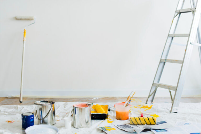 Lege kamer met witte muur die geverfd wordt. Op de grond bevinden zich een ladder en schilderspullen.