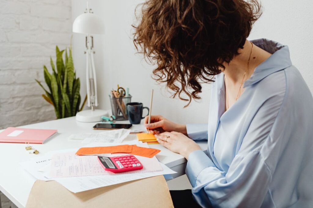 Een vrouw die aan een bureau rekenwerk doet met een rekenmachine.