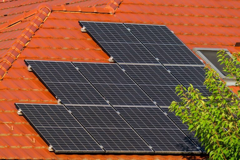 Ingezoomde foto's van een paar zonnepanelen op het rood dak van een huis.