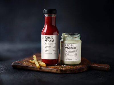 M&S tomato ketchup and olive oil mayonnaise in ingredient-led packaging, displayed on a wooden serving board.