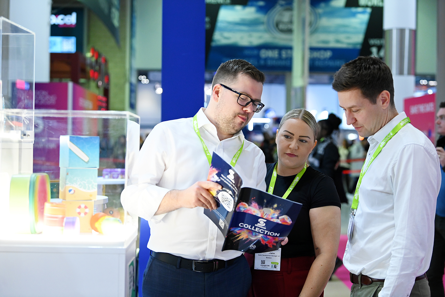 Packaging professionals discussing product samples and marketing materials at an exhibitor stand during London Packaging Week.