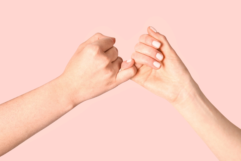 Two hands linking little fingers in a pinky promise gesture, symbolising trust and commitment.