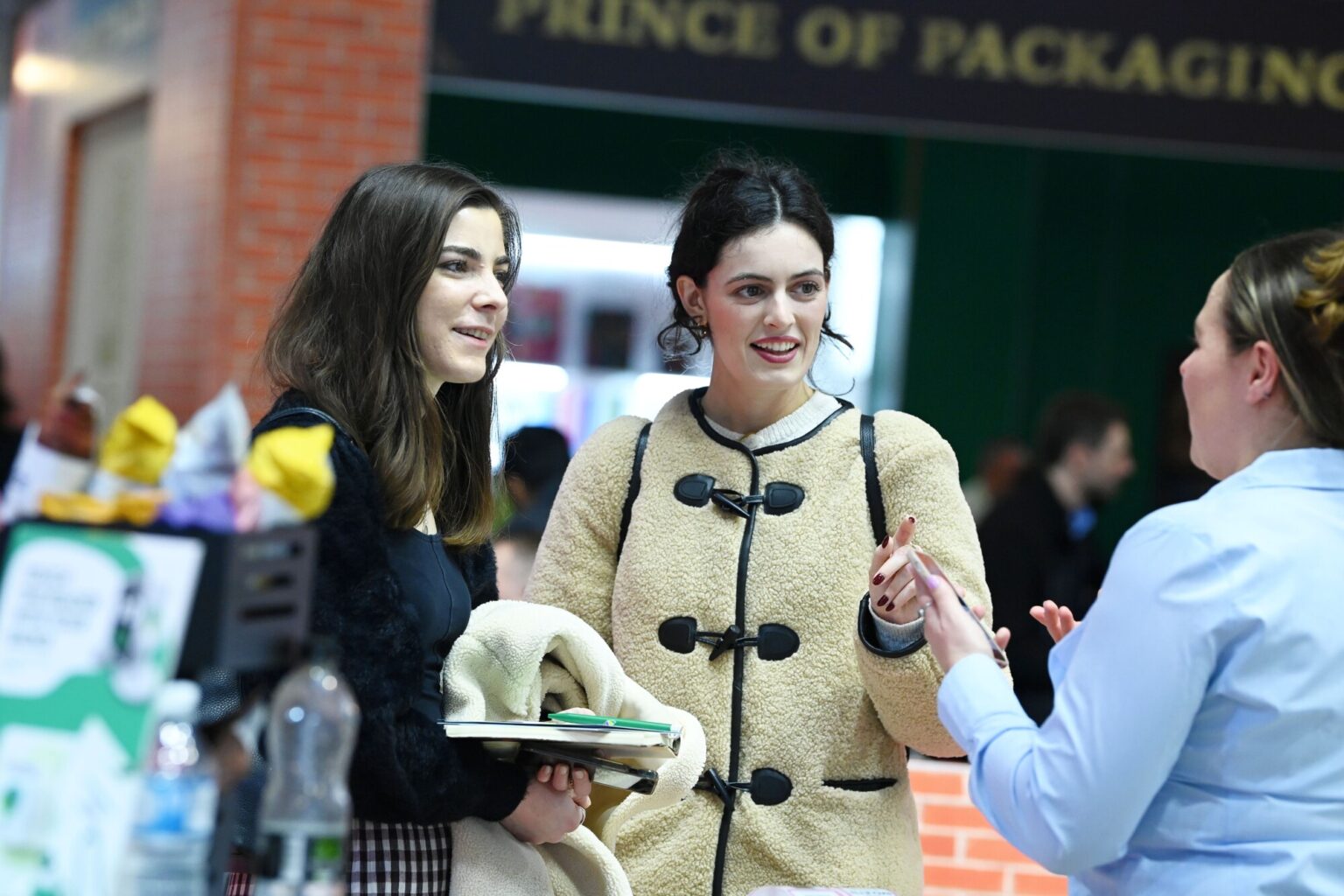 Two visitors speaking with an exhibitor on the busy exhibition floor at Packaging Innovations & Empack.