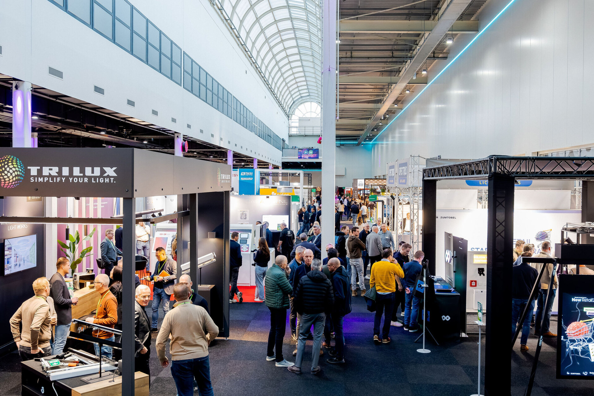 Bezoekers op drukke verlichtingsvakbeurs tussen exposantenstands